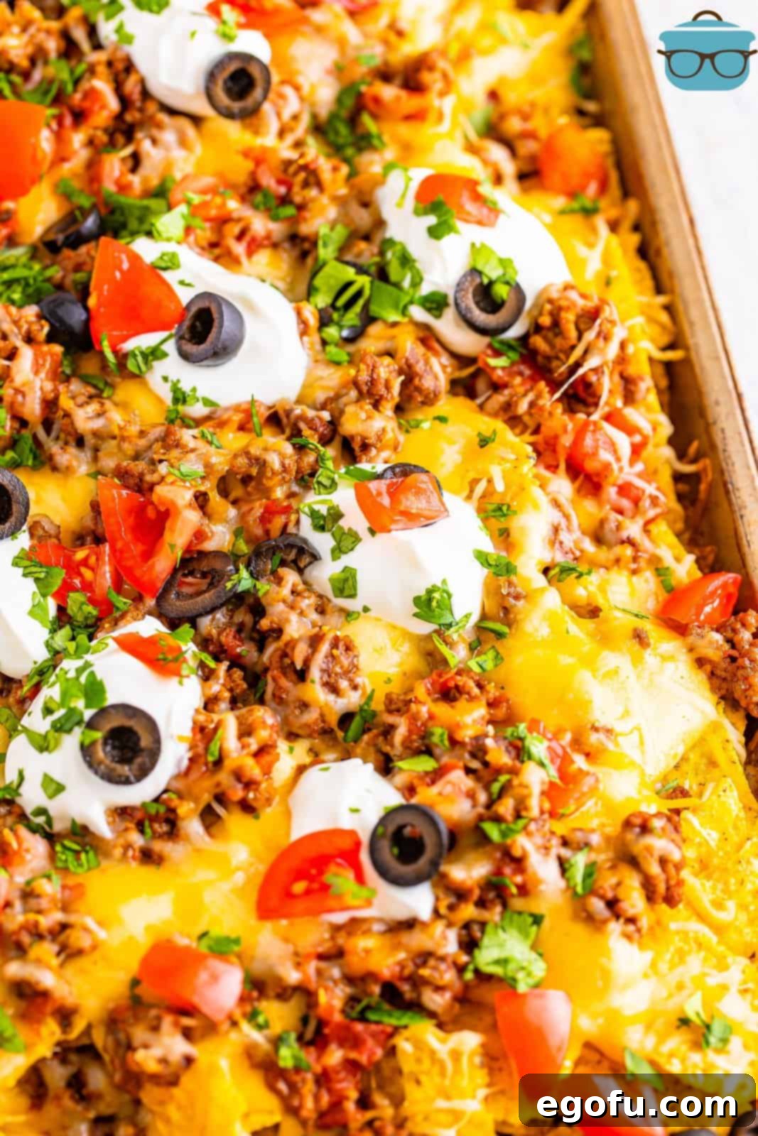 Close up view of the finished Sheet Pan Nachos, beautifully adorned with fresh toppings like diced tomatoes, sour cream, black olives, and cilantro.