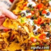 Close up looking at nachos and a hand holding a loaded nacho chip.