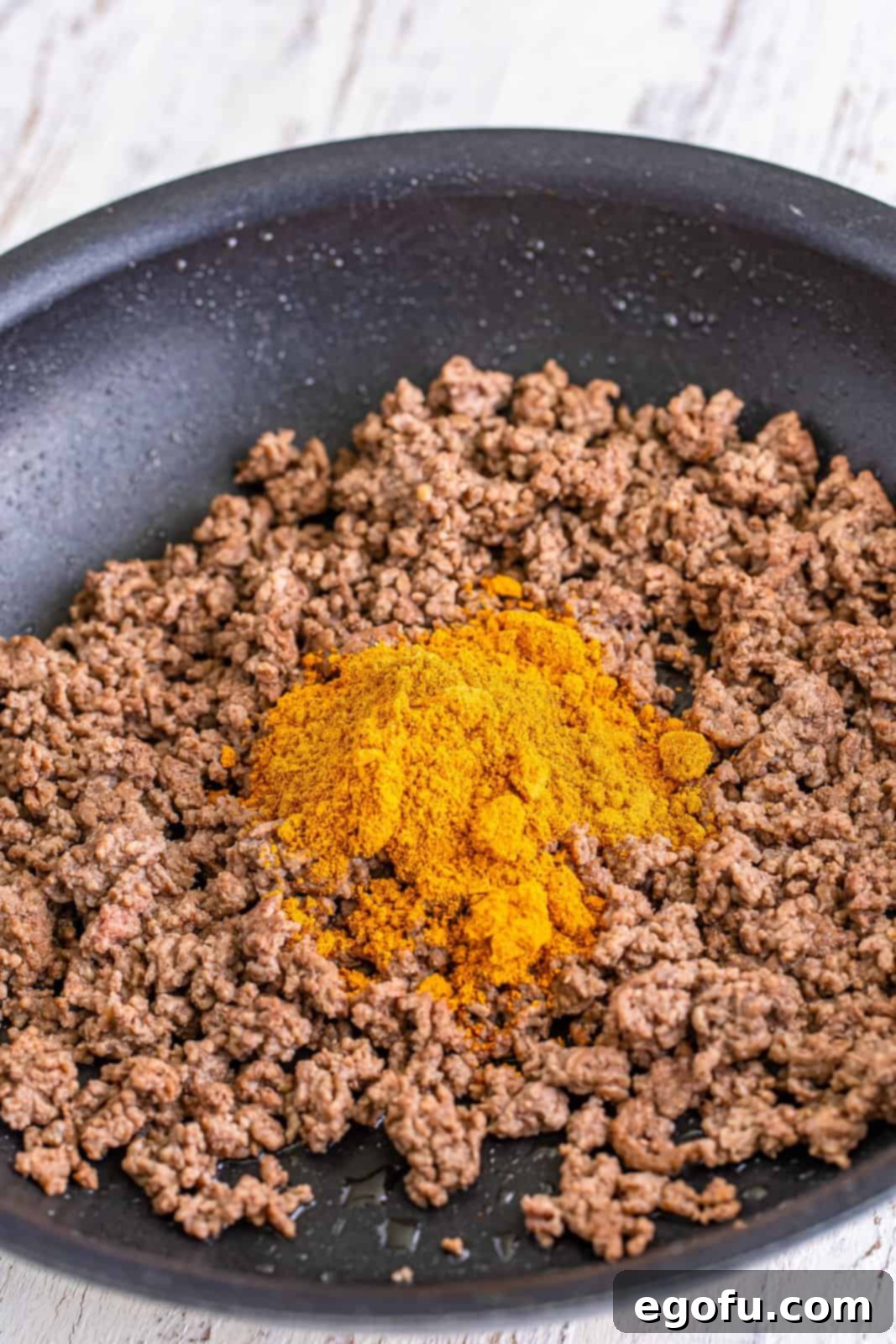 Cooked ground beef in a skillet, now mixed with vibrant taco seasoning.