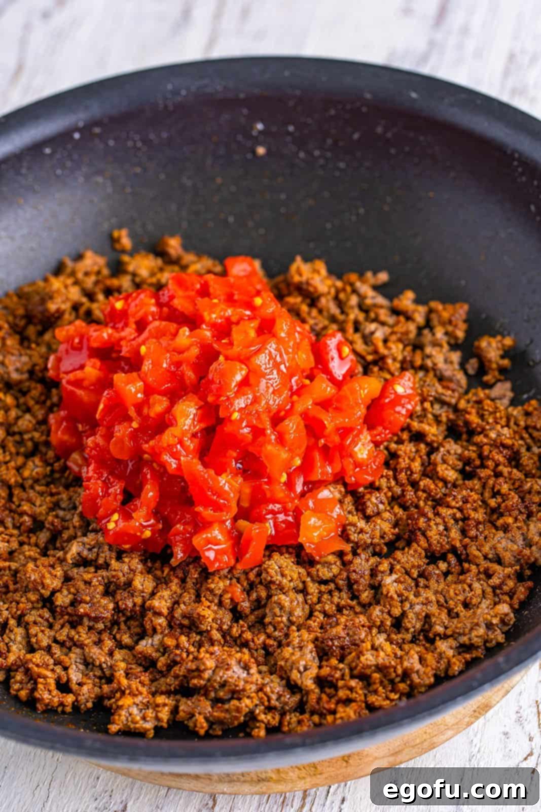 Rotel tomatoes and green chilies expertly mixed into the seasoned ground beef in a skillet.