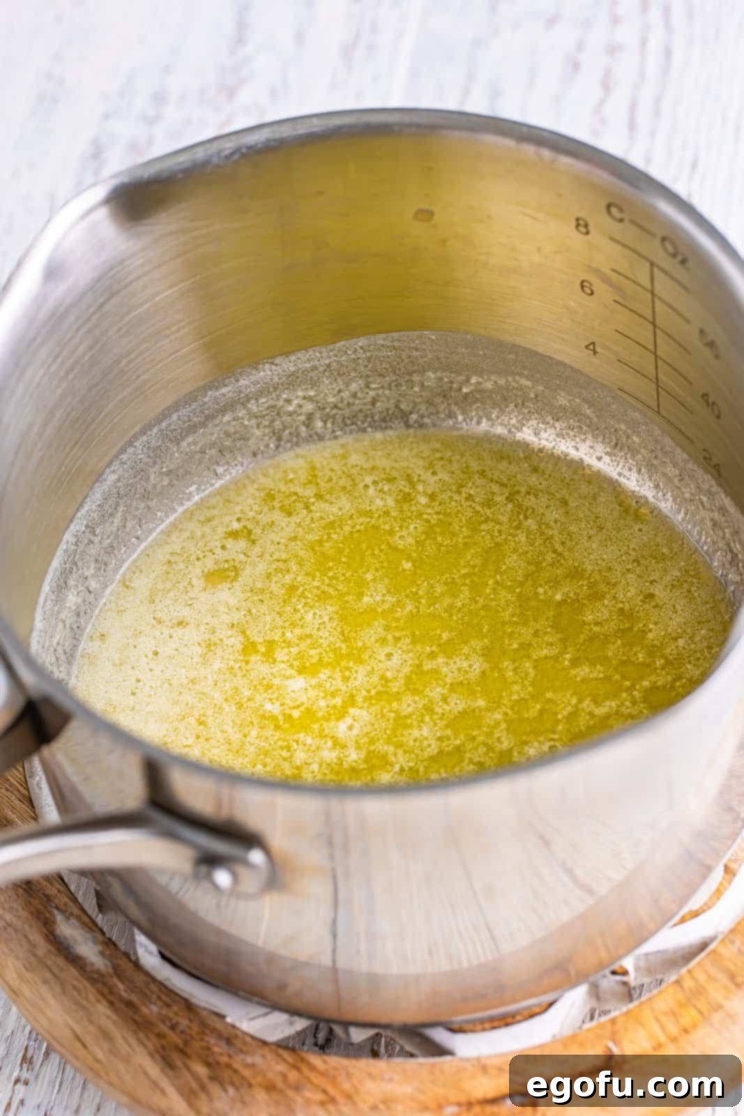 A medium saucepot on the stovetop containing perfectly melted butter, beginning the cheese sauce creation.