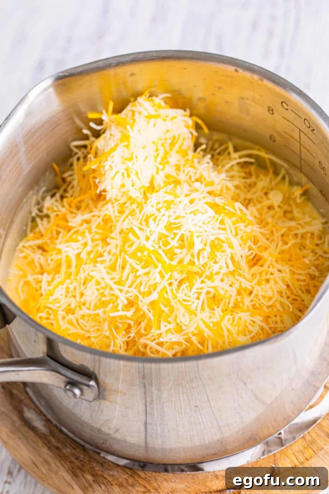 Shredded Mexican blend cheese melting into a creamy sauce in a saucepot, forming the homemade cheese sauce.