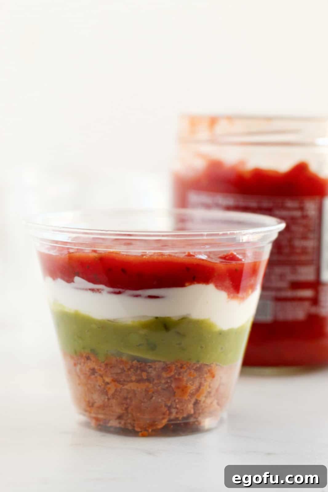 Small plastic cup with refried beans, guacamole, sour cream, and salsa.