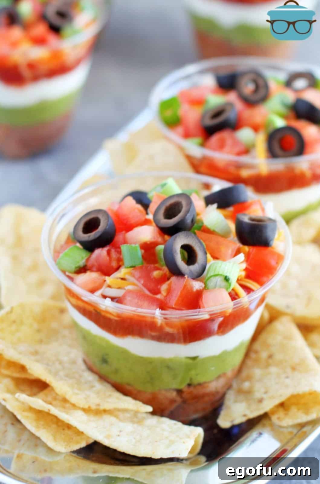 Two cups of 7 layer dip with chips on a serving plate.