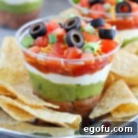 Seven layer dip in clear plastic cups with chips on a cup.