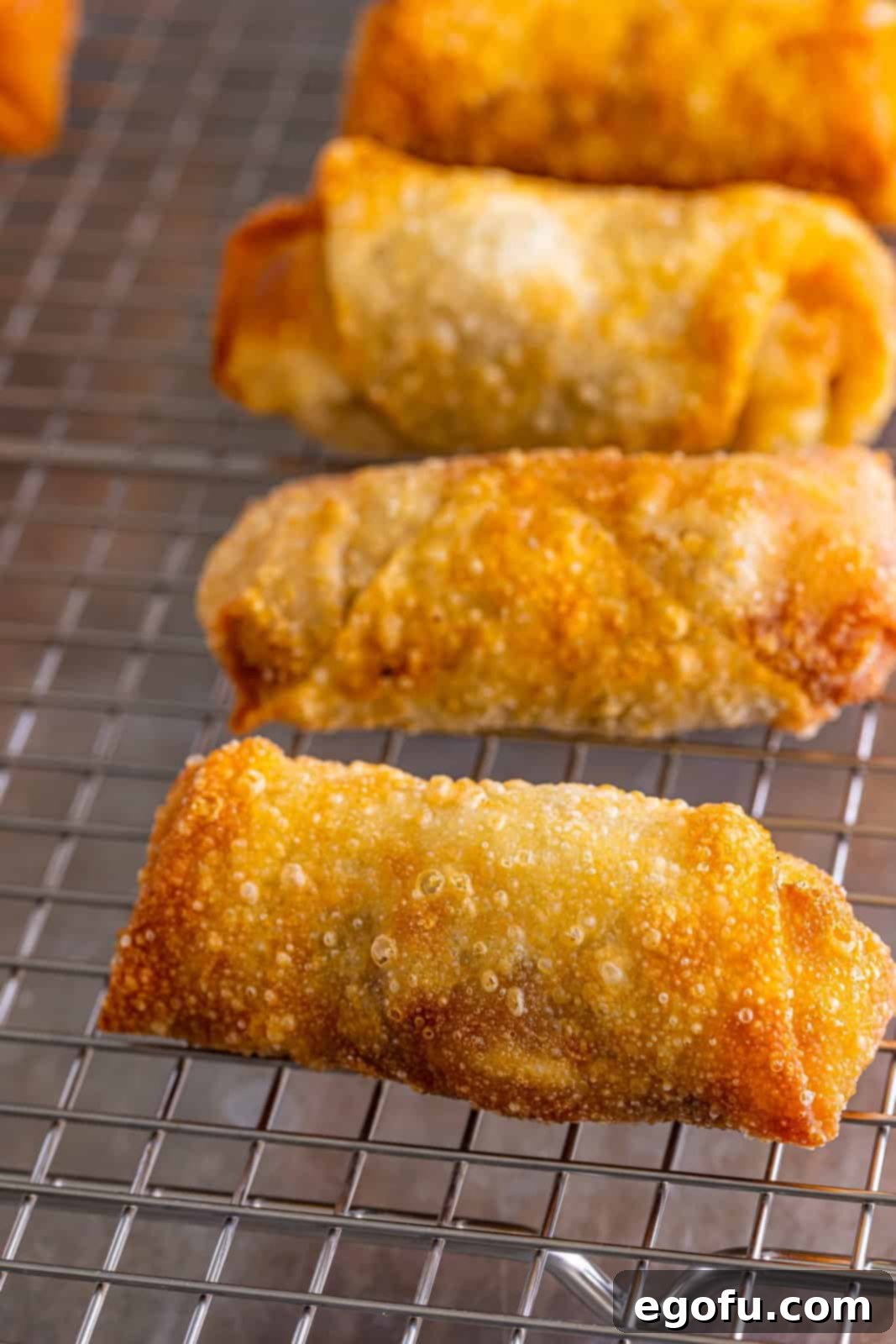 A few freshly fried, golden French Dip Egg Rolls resting on a wire rack to maintain crispness.
