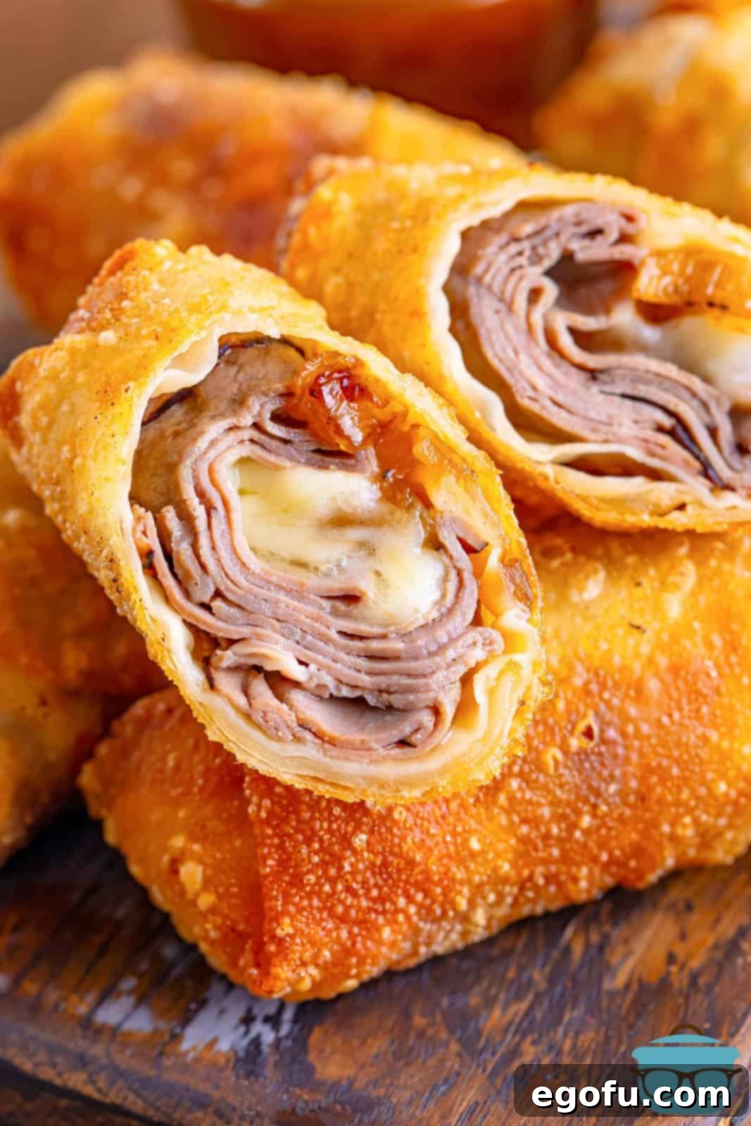 A stack of perfectly fried French Dip Egg Rolls on a white platter, ready to be served.