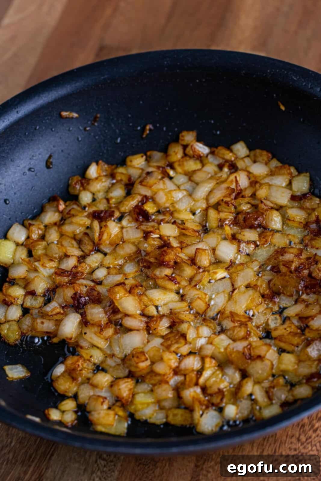A skillet filled with golden-brown, cooked onions, seasoned with pepper and sugar, and sautéd in butter.