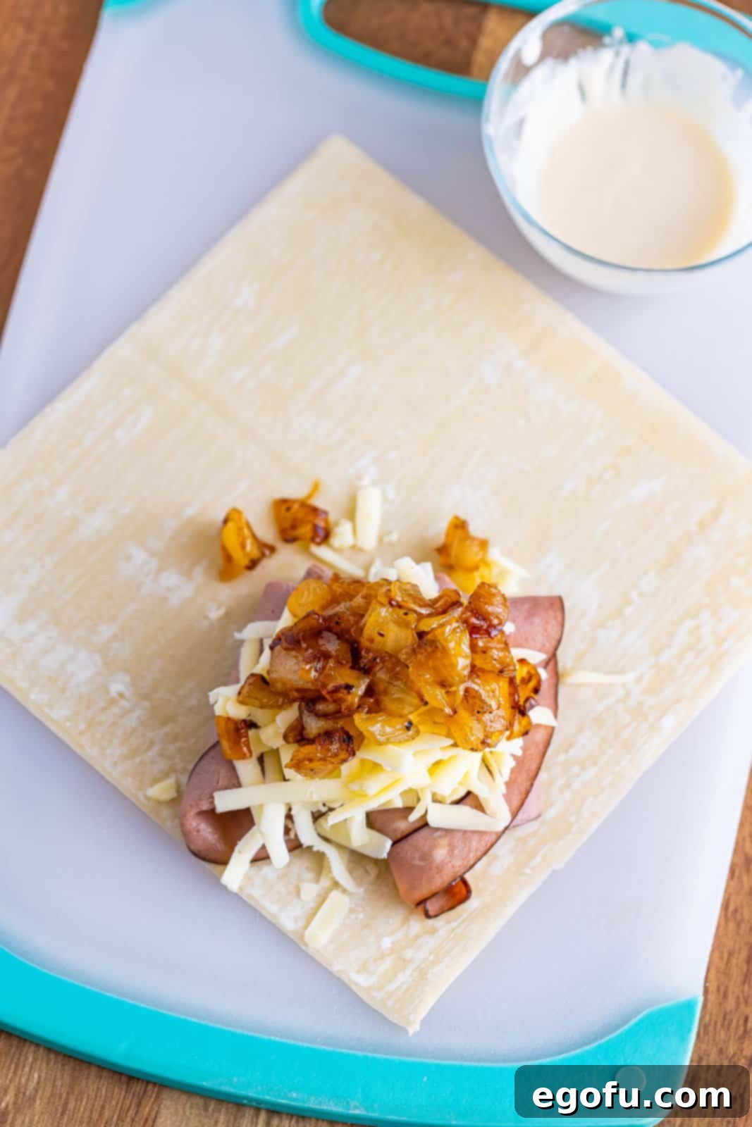 An egg roll wrapper with roast beef, shredded provolone cheese, and a spoonful of cooked, caramelized onions on top.