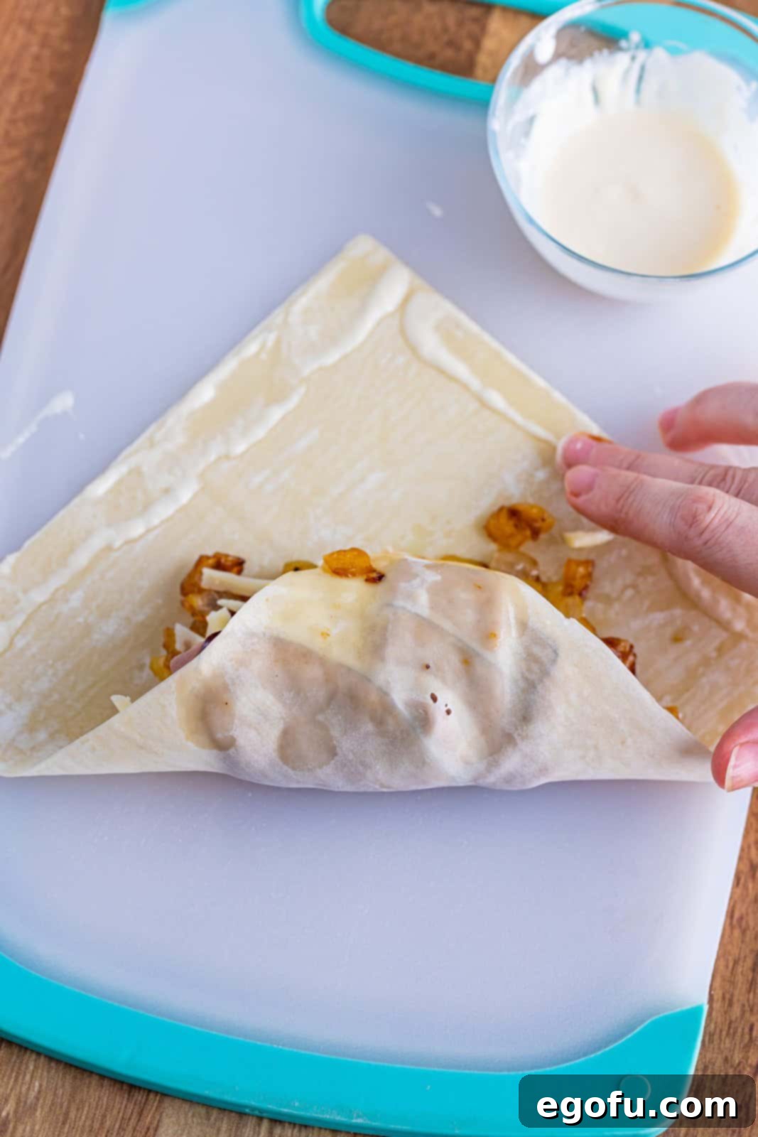 A French Dip Egg Roll in the process of being rolled up, with the bottom corner folded over the filling and the sides prepared for tucking.
