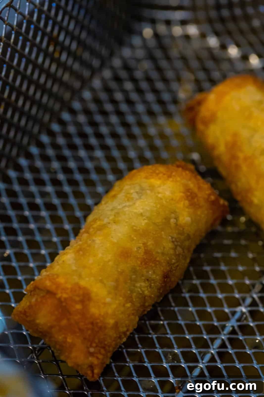 A fryer basket lifting several golden brown, crispy French Dip Egg Rolls from hot oil.