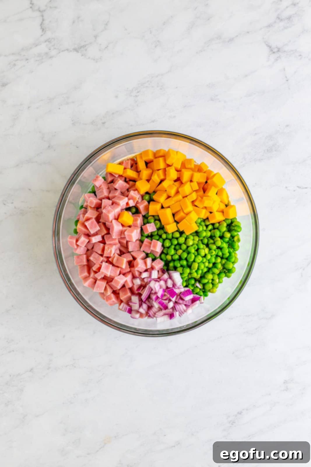 Creamy Garden Pea Salad 6 A mixing bowl with ham, cheese, onion, and peas.