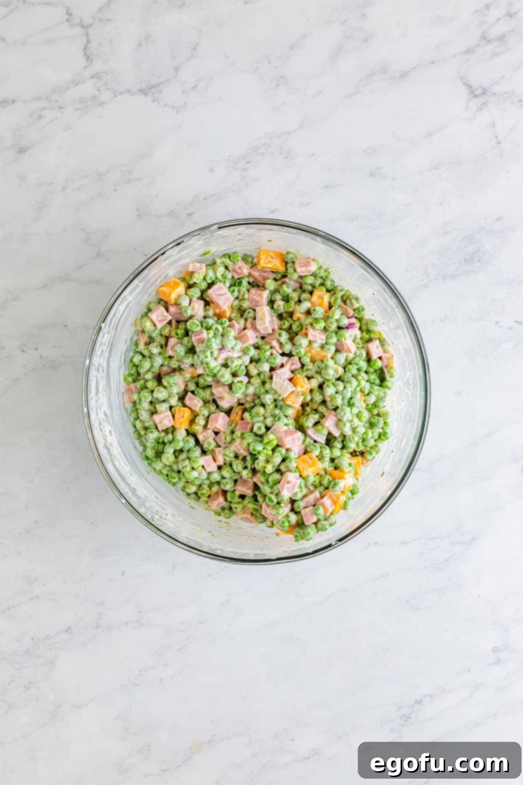 Creamy Garden Pea Salad 7 A mixing bowl with the dressing over the peas, ham, cheese, and onion.