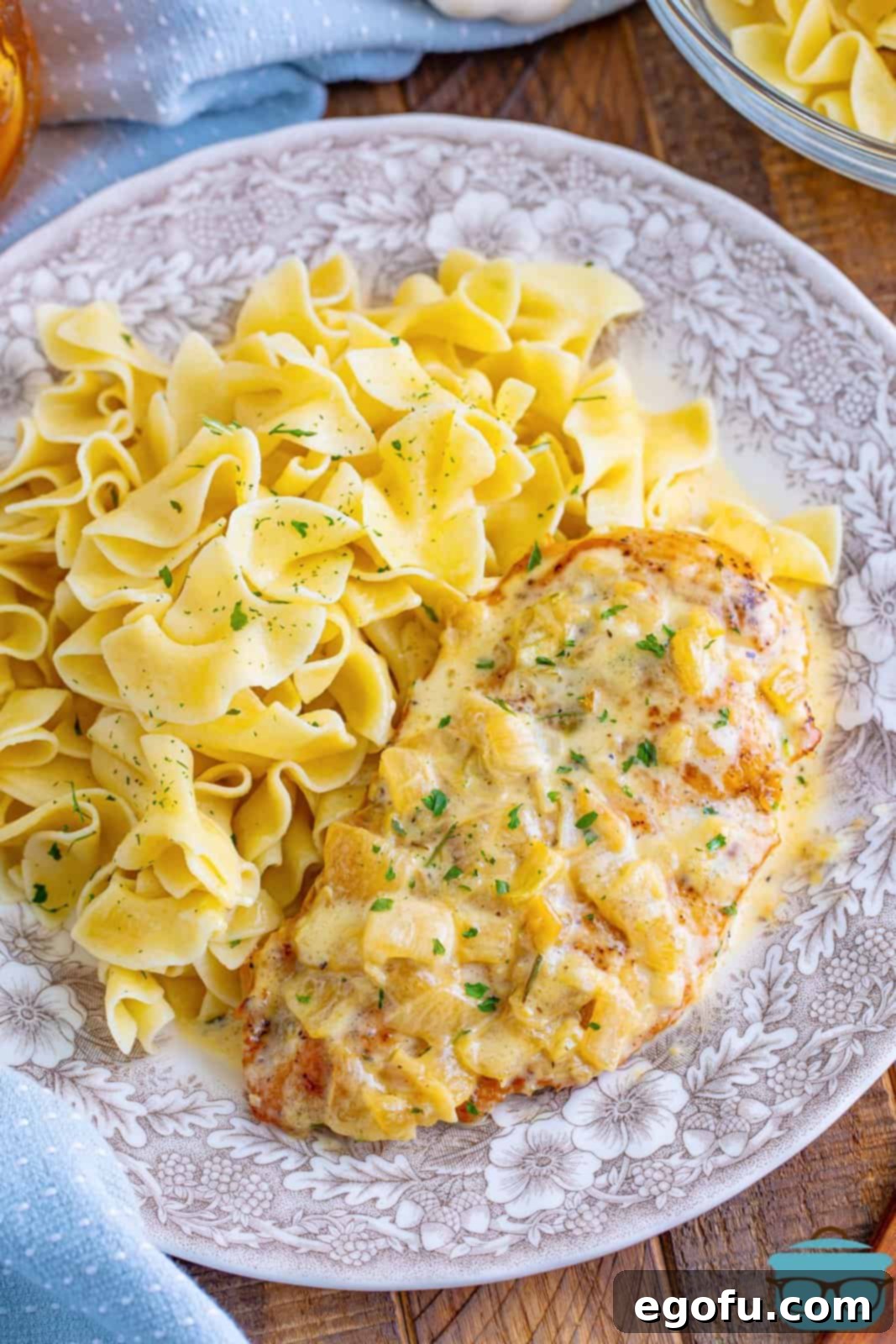 A decorative plate with creamy chicken with a side of pasta.
