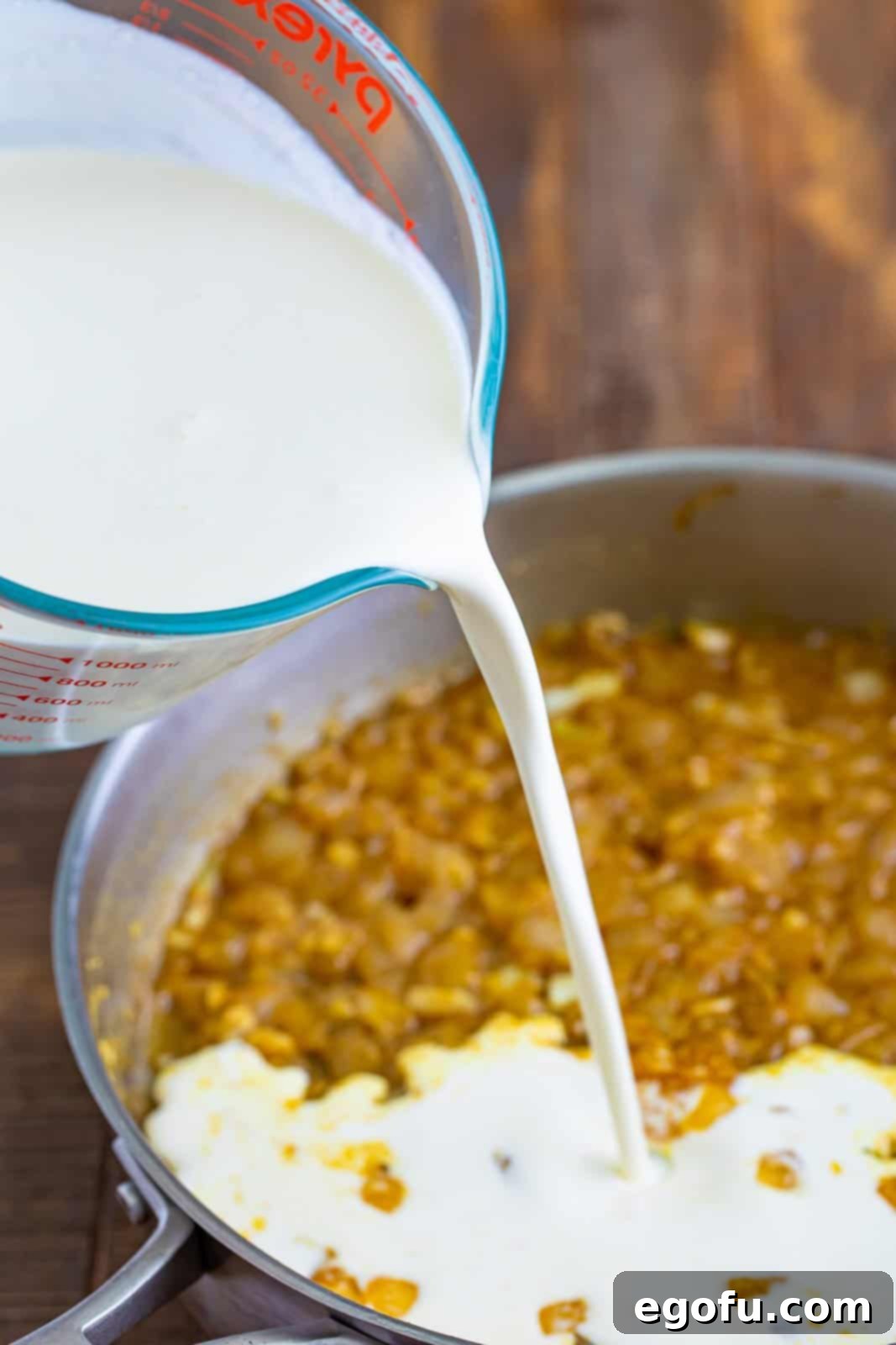 Heavy cream being poured in a saucepan of other ingredients for creamy chicken sauce.