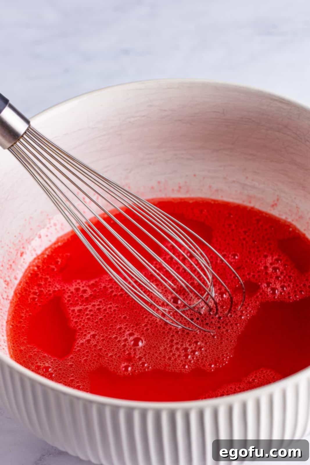 A mixing bowl with strawberry banana jello and water. 