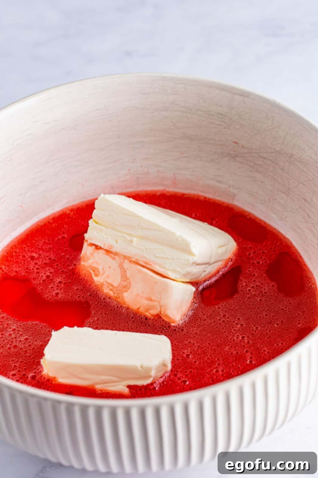 A mixing bowl with strawberry banana jello and cream cheese. 