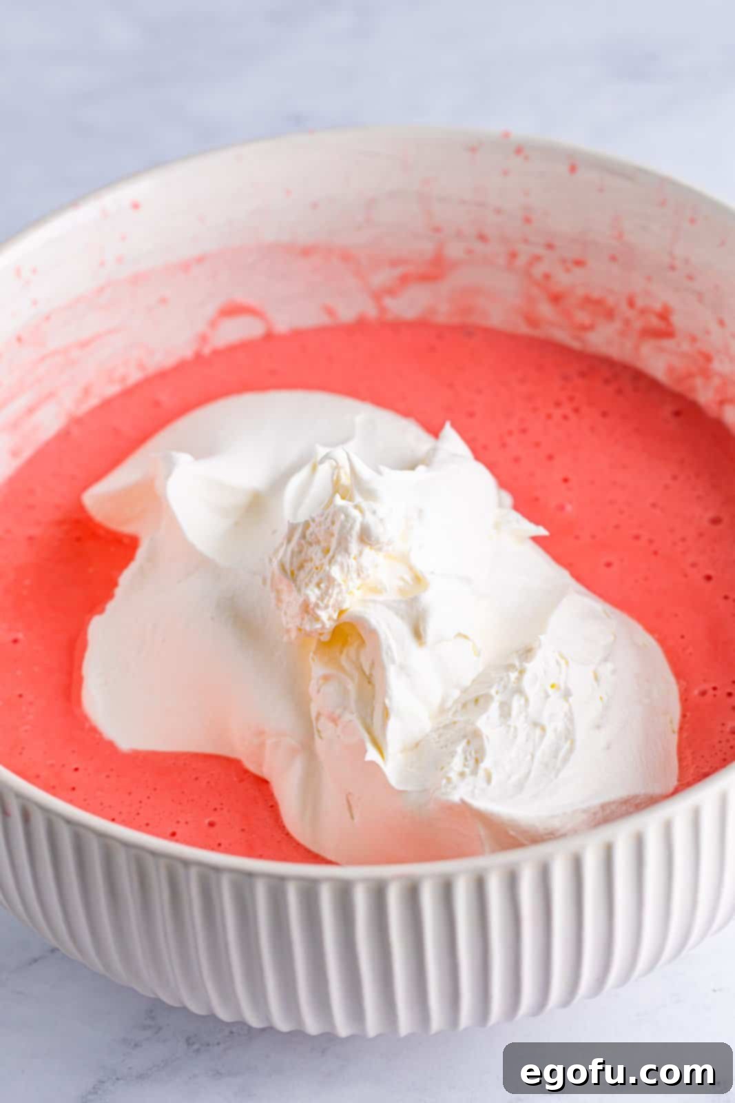 A mixing bowl with strawberry banana jello, whipped topping, and cream cheese. 
