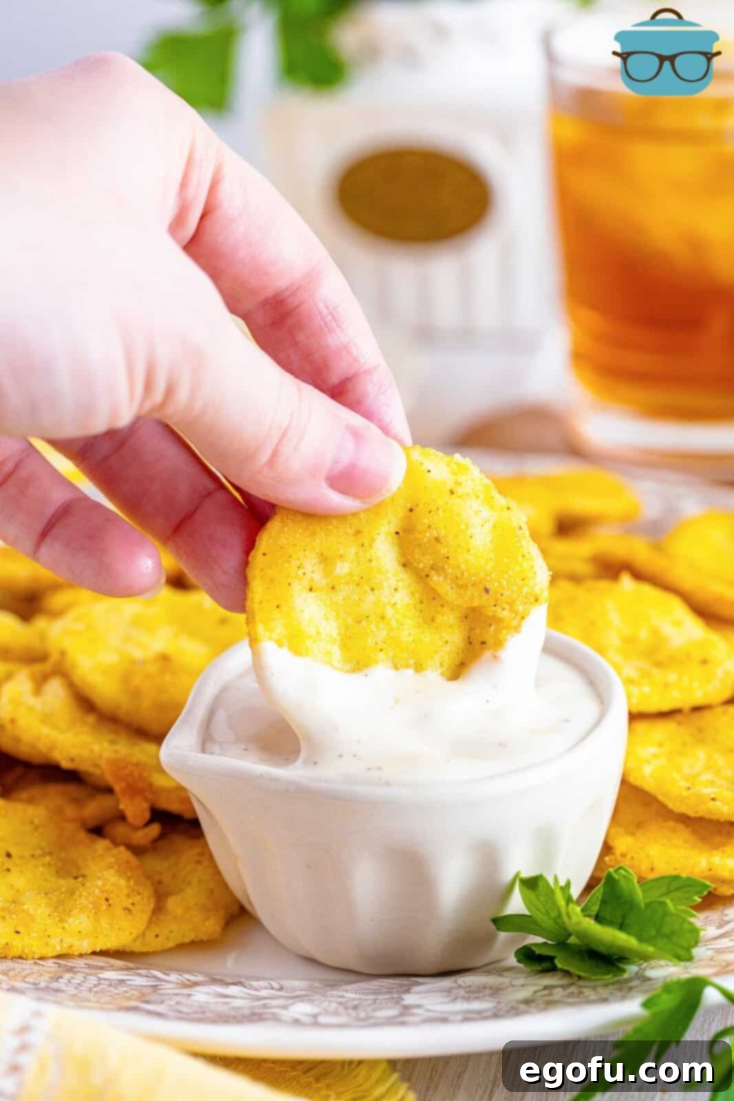 Down Home Fried Squash 10 A hand dipping a piece of crispy fried squash into a bowl of ranch dressing.
