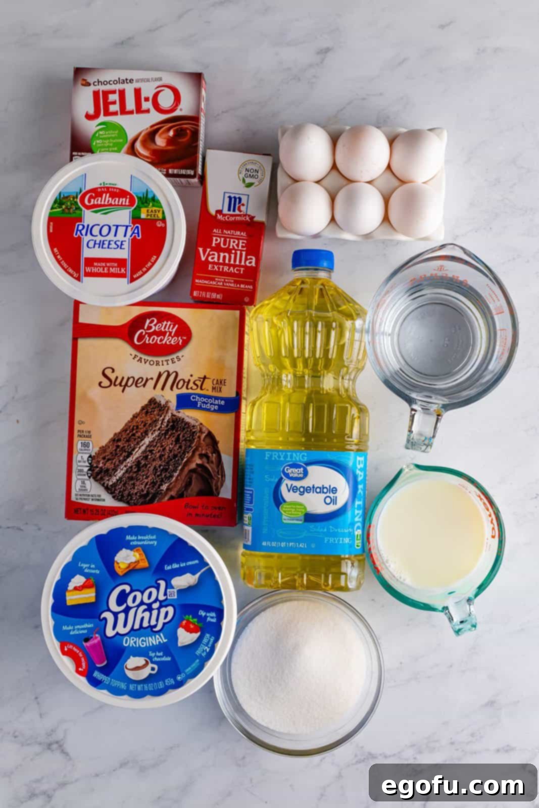 Amore Italian Dream Cake 4 A vibrant flat lay of all the Italian Love Cake ingredients: Cool Whip, chocolate cake mix, chocolate pudding mix, fresh eggs, cold milk, vegetable oil, water, granulated sugar, pure vanilla extract, and a container of creamy ricotta cheese.