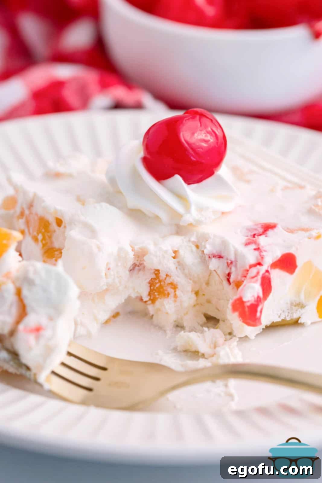 A plate with a serving of frozen fruit salad, garnished with a maraschino cherry on top, showcasing its creamy texture and colorful fruit pieces.