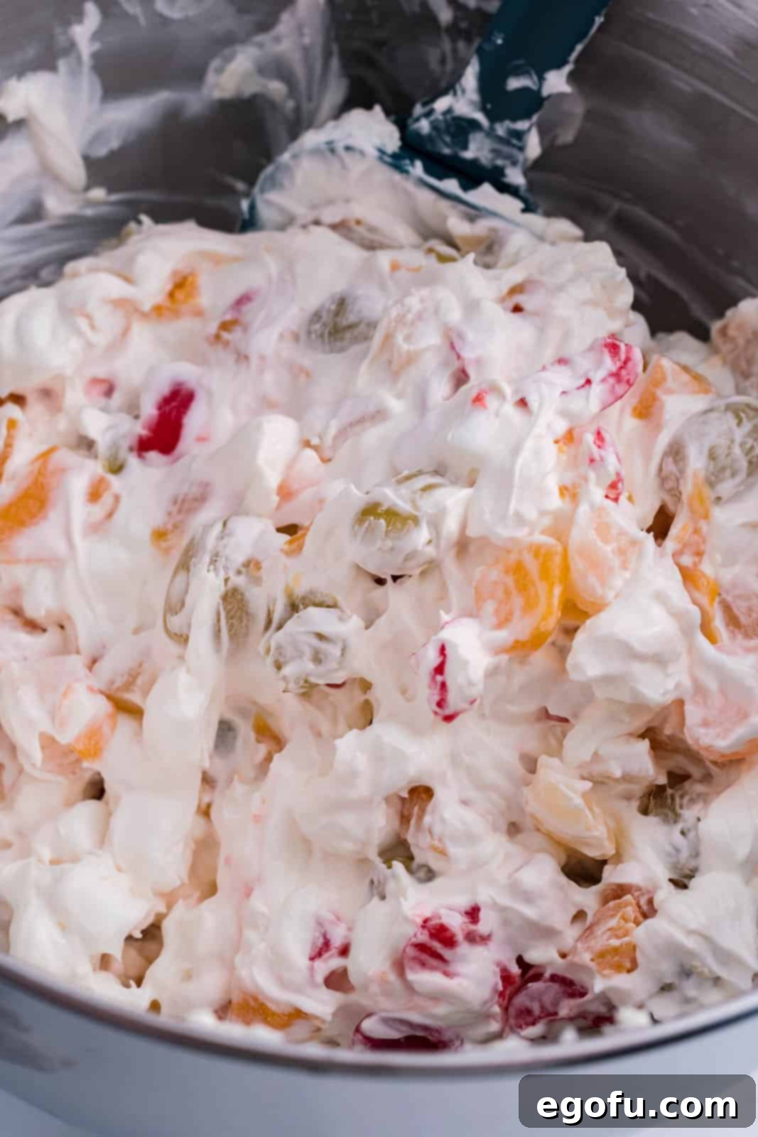 A large mixing bowl containing the combined ingredients for frozen fruit salad: cream cheese mixture, fruit cocktail, marshmallows, and cherries, ready to be mixed.
