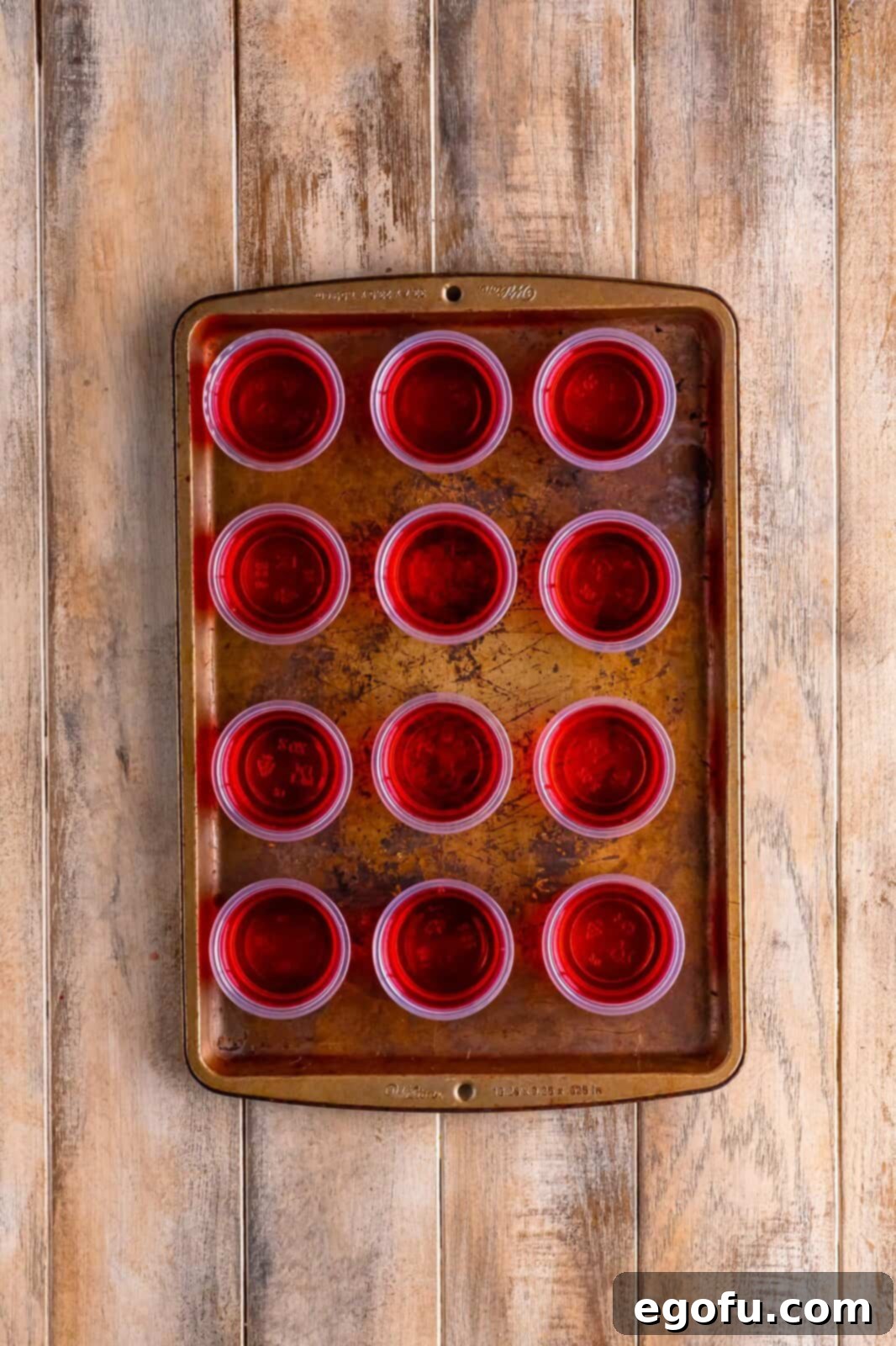 A baking tray of jello shot cups filled up with jello. 