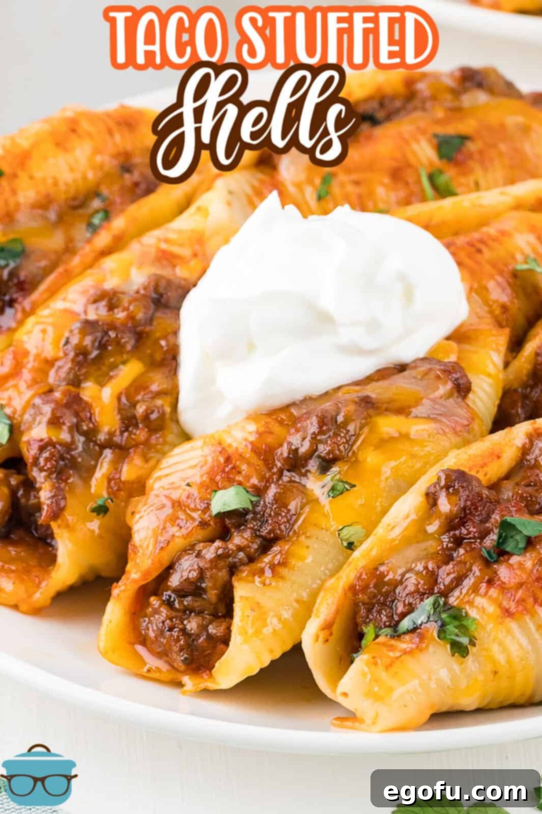 A dollop of sour cream sitting on top of a serving of taco stuffed shells on a white plate, garnished with fresh cilantro.