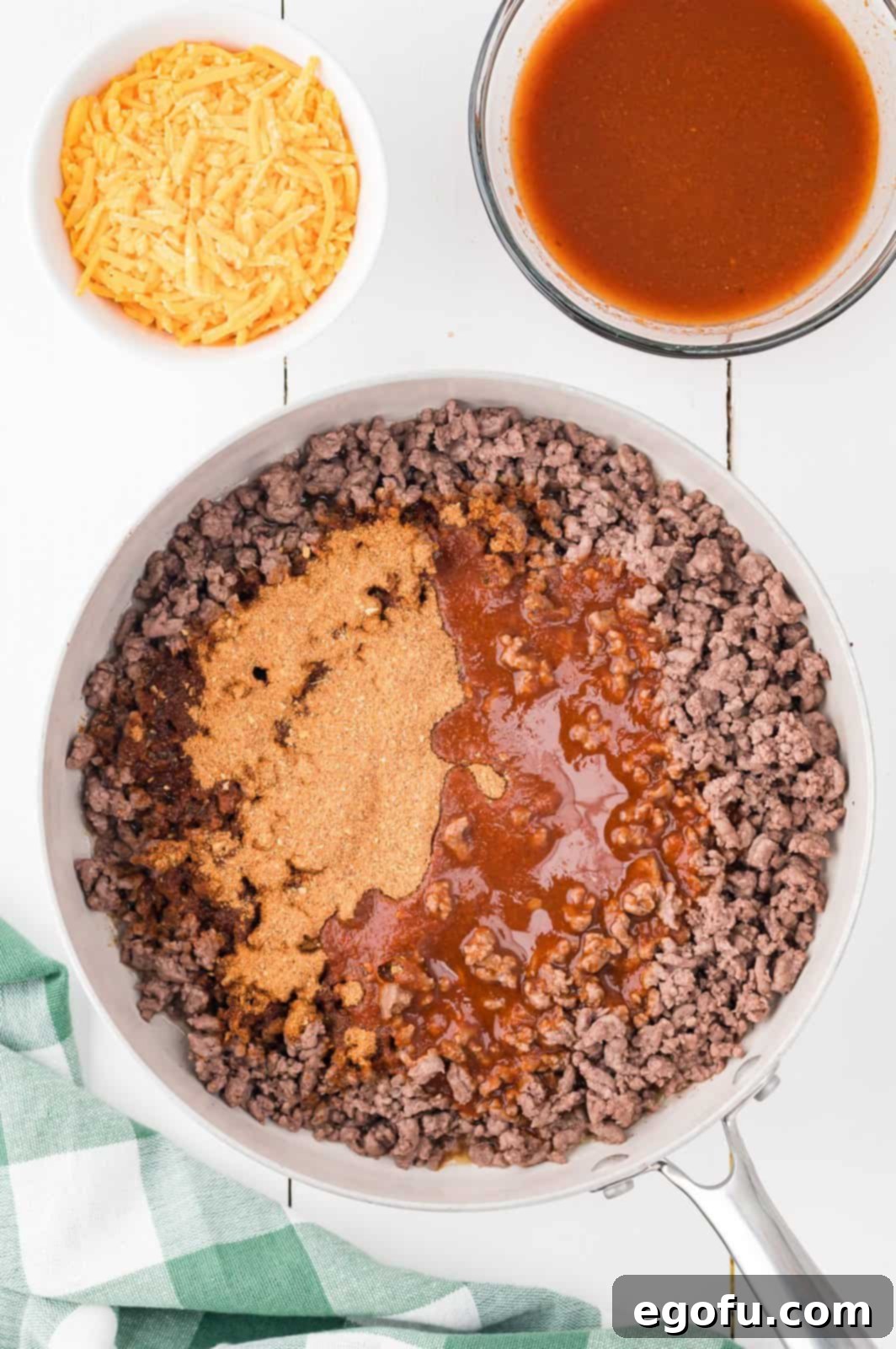 A skillet filled with cooked ground beef, now simmering with taco seasoning and a vibrant red enchilada sauce.
