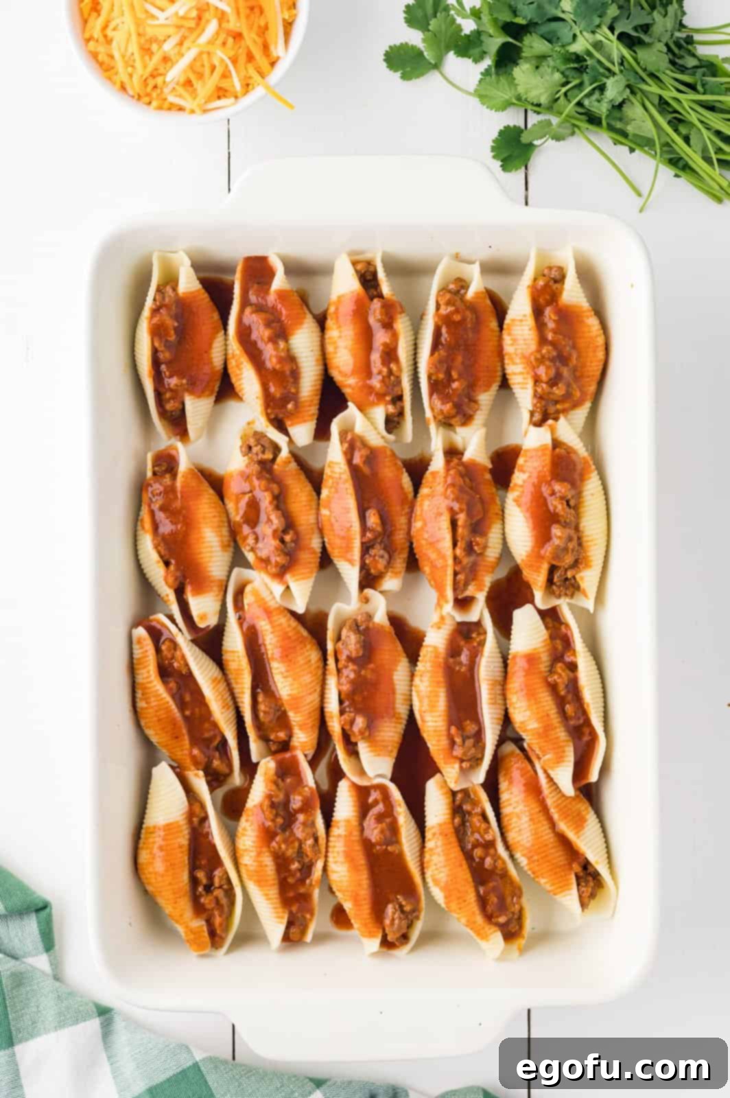 Stuffed shells in a baking dish, now generously covered with the remaining enchilada sauce, creating a rich base for the cheese.