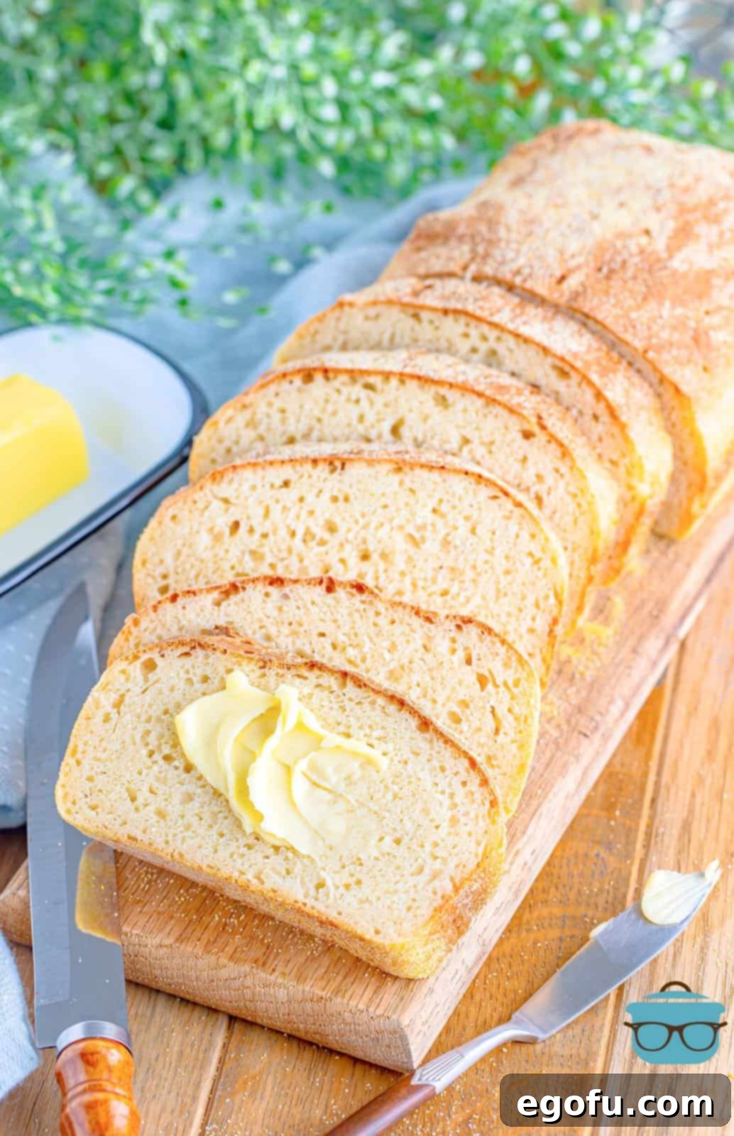 slices of English Muffin Bread on a wooden cutting board with one slice slathered with butter.
