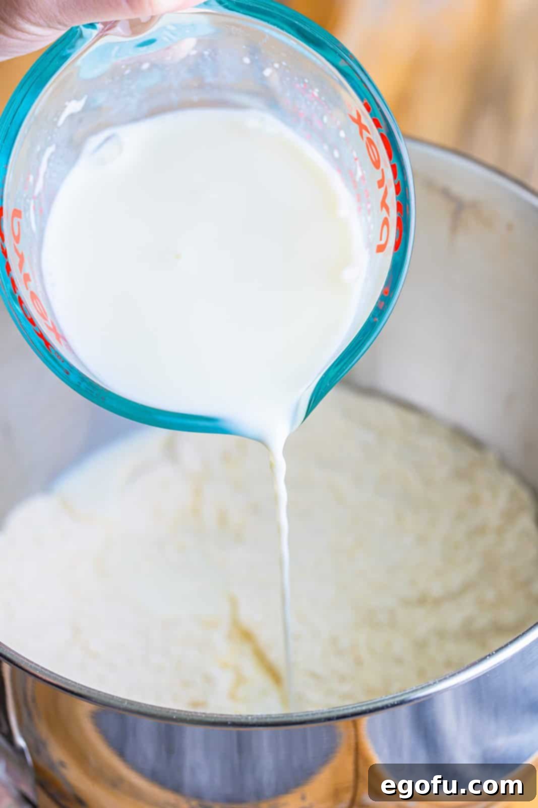 warm milk being poured into flour in a mixing bowl.