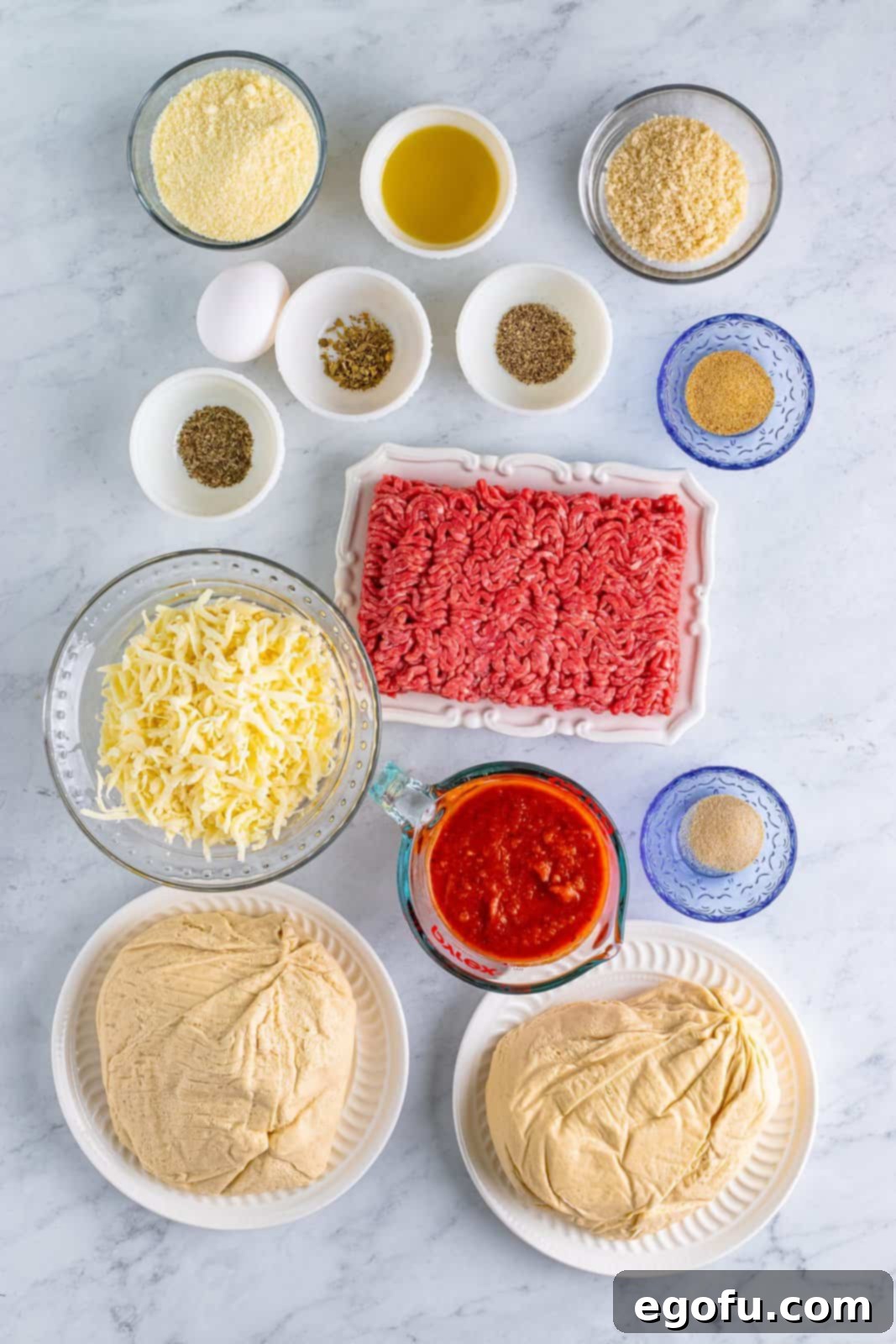 A vibrant flat lay of all the essential ingredients: Ground beef, egg, grated parmesan cheese, panko breadcrumbs, garlic powder, onion powder, black pepper, dried basil, dried oregano, pizza dough, olive oil, pizza sauce, and shredded mozzarella cheese.