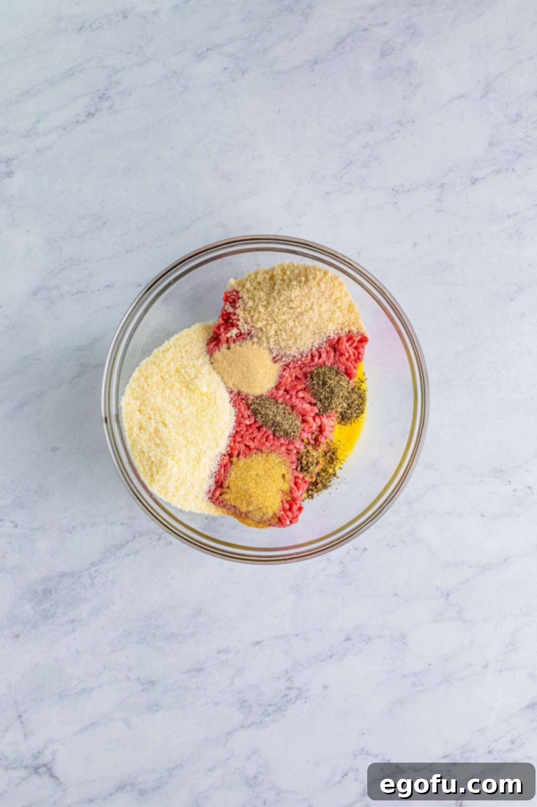 A mixing bowl filled with the raw meatball mixture: ground beef, egg, Parmesan cheese, breadcrumbs, garlic powder, onion powder, black pepper, basil, and oregano, ready to be formed.