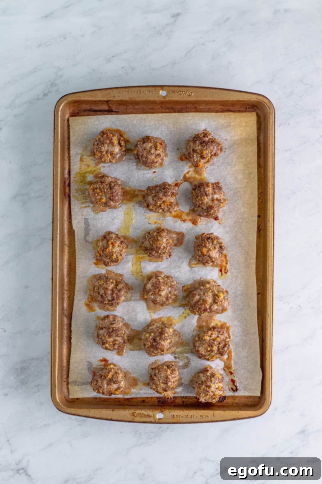Fully cooked, golden brown meatballs resting on a parchment paper lined baking sheet, ready for the next step.