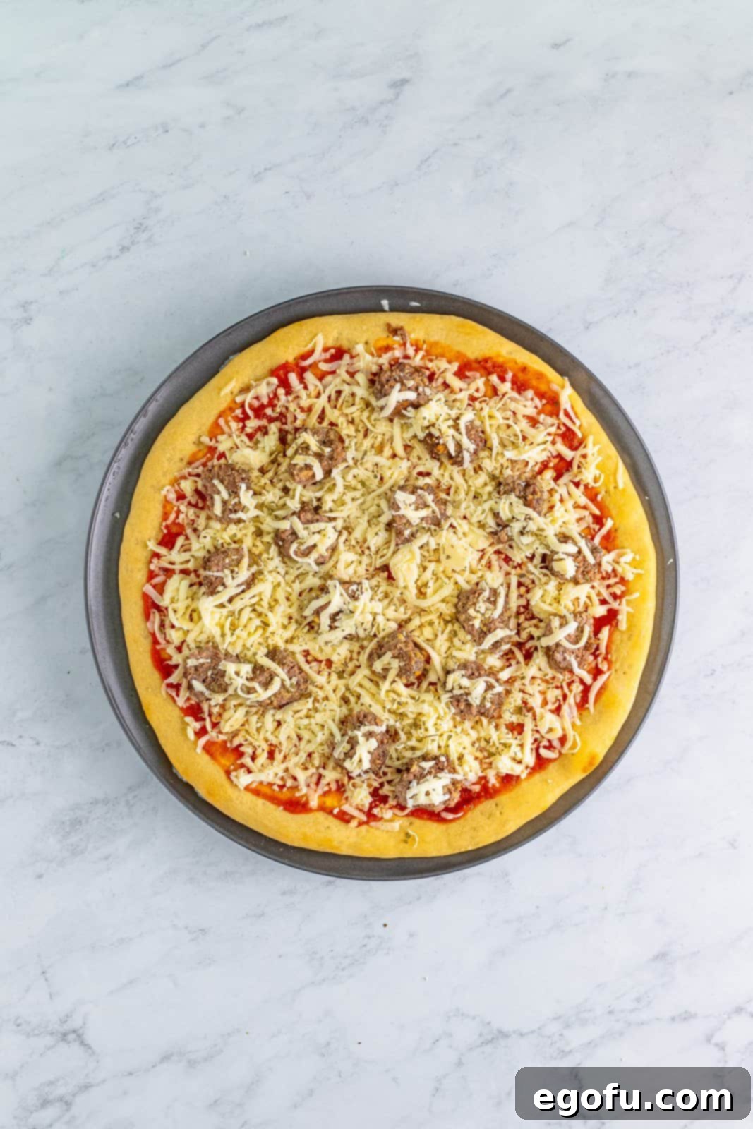 An uncooked meatball pizza, showcasing the layers of sauce, cheese, and halved meatballs before final baking.