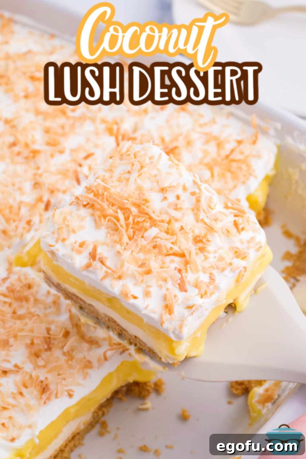 A serving utensil lifts a perfectly cut slice of Coconut Cream Lush from a baking dish.