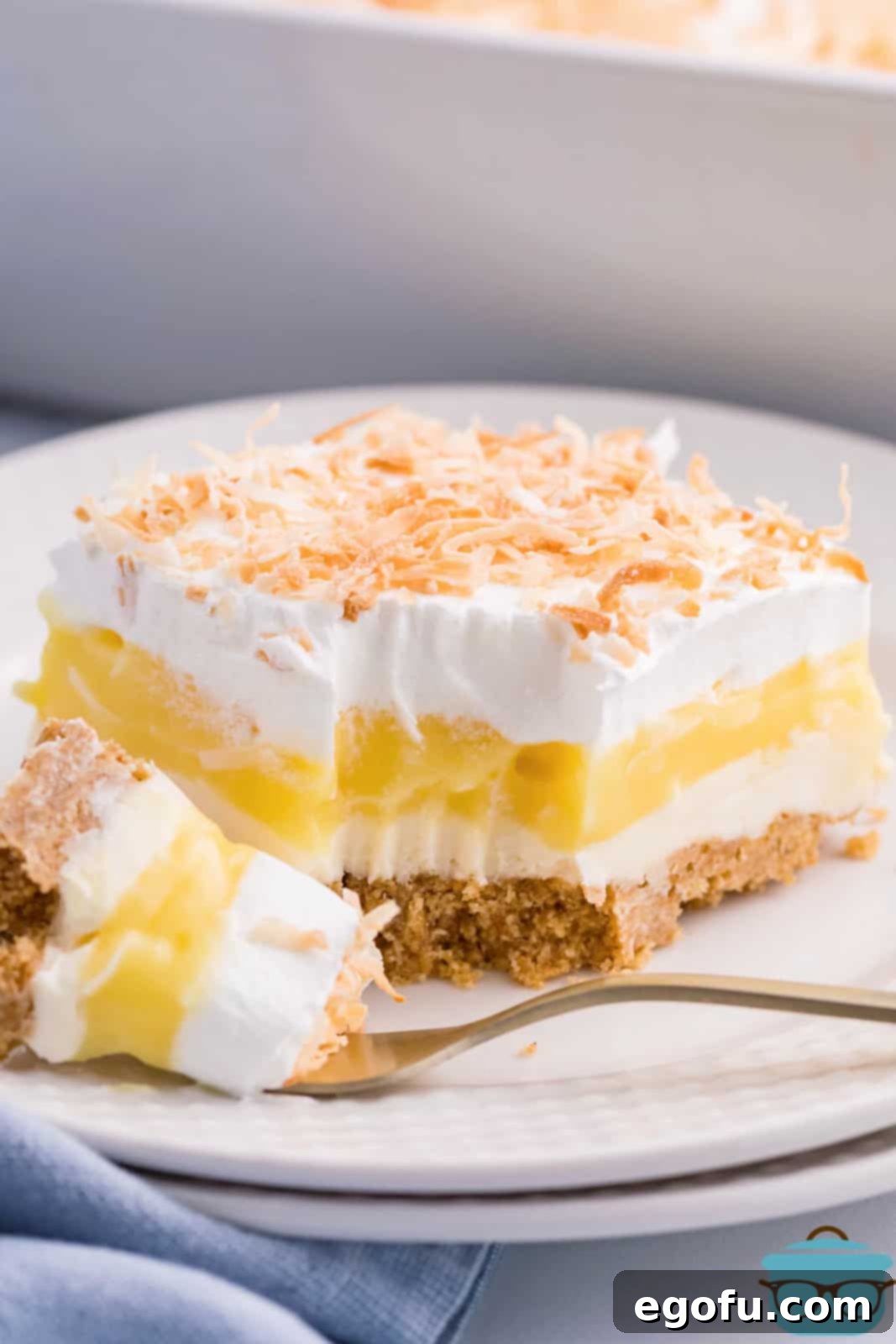A close-up of a fork holding a bite of Coconut Cream Lush, with a full slice of the dessert visible in the background.