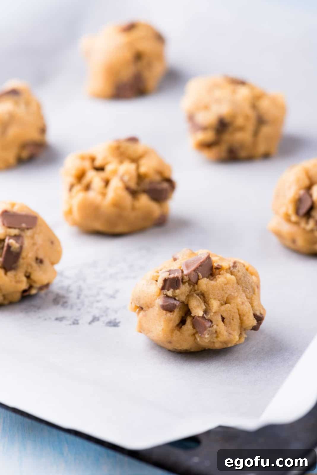 Raw cookie dough balls evenly spaced on a baking tray lined with parchment paper, ready for flash freezing.