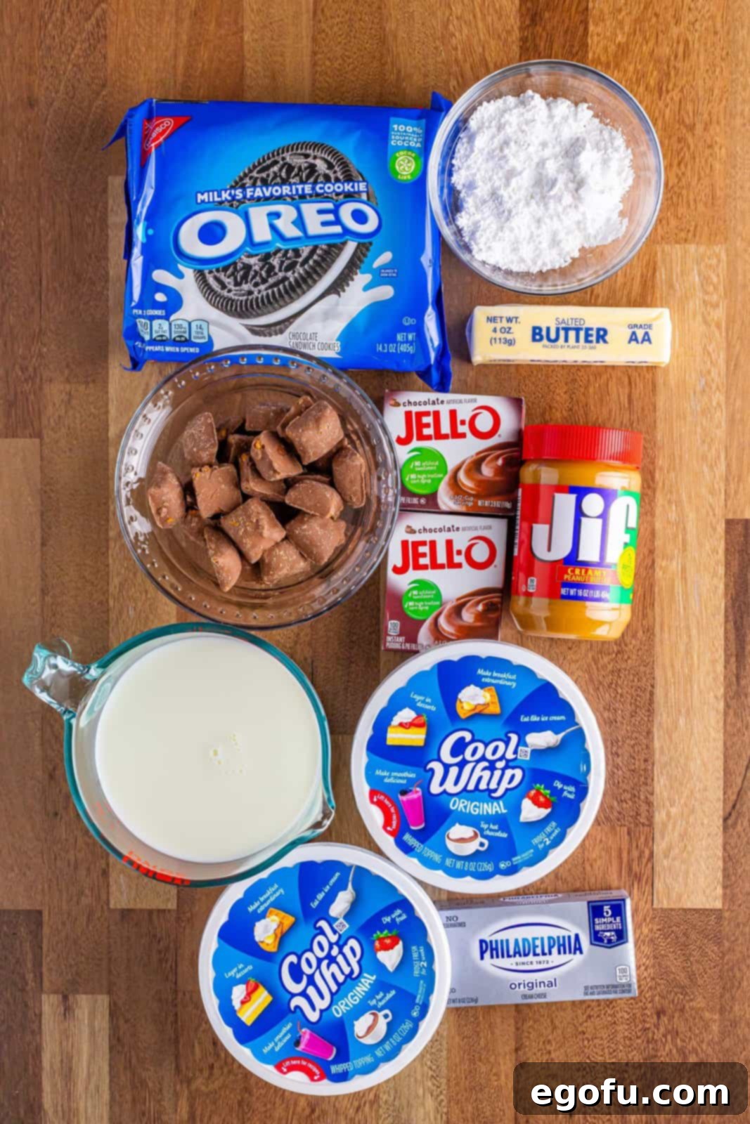 Golden Butterfinger Dream 3 A flat lay photograph of all the ingredients needed for Butterfinger Lush: Oreos, butter, cream cheese, powdered sugar, creamy peanut butter, mini Butterfinger bars, Cool Whip, milk, and chocolate pudding mix, neatly arranged.