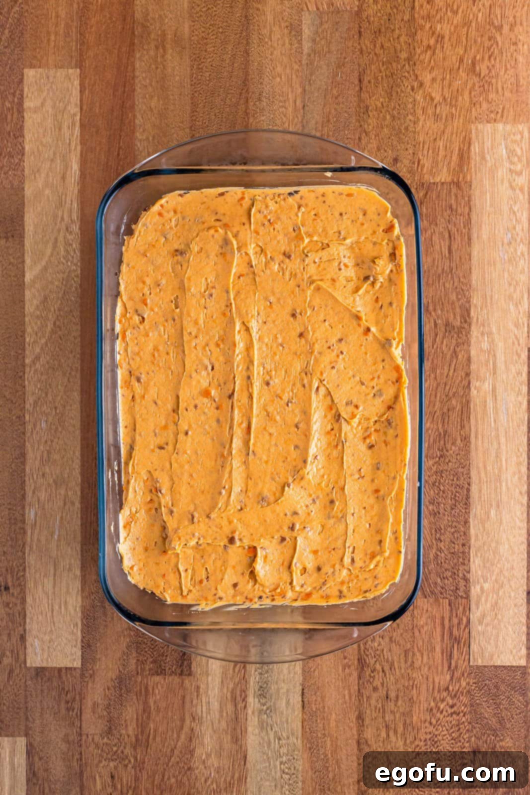 Golden Butterfinger Dream 9 The smooth peanut butter and cream cheese layer spread evenly on top of the dark Oreo crust in a baking dish.