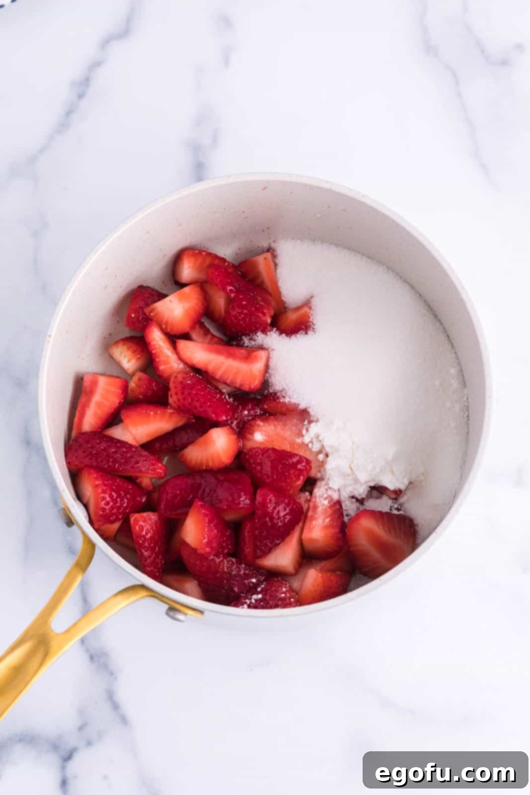 A saucepan with strawberries and sugar being stirred.