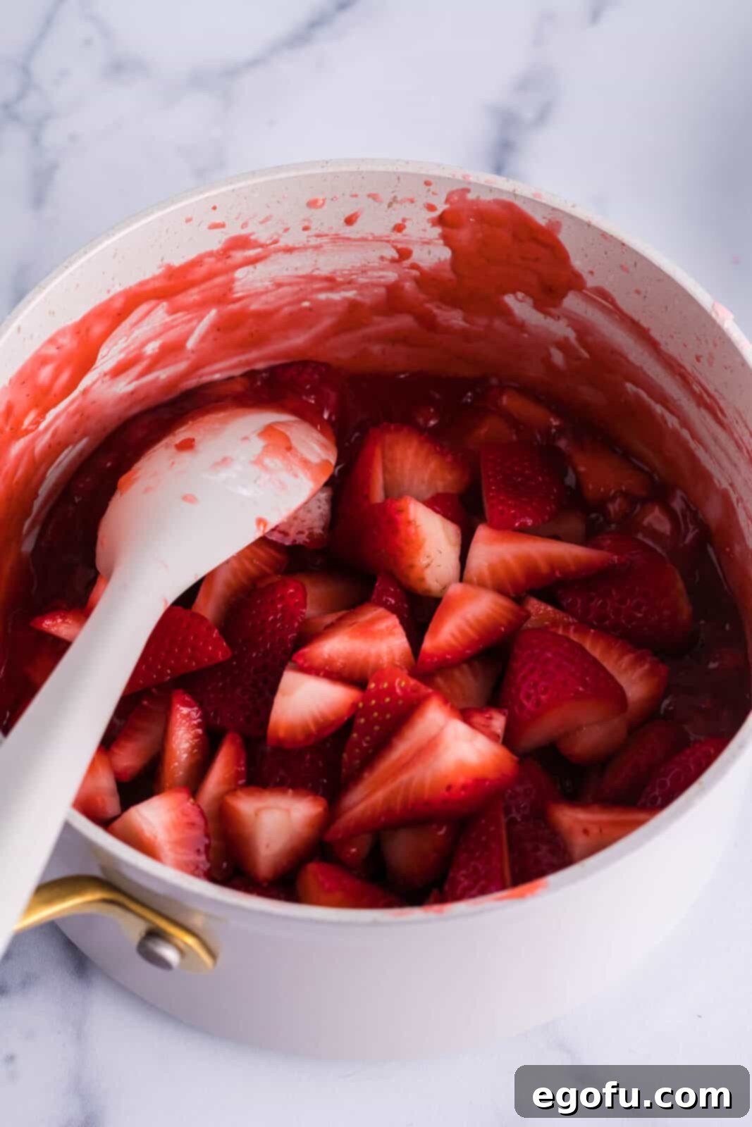 A saucepan with mashed strawberries and a thickening sauce.