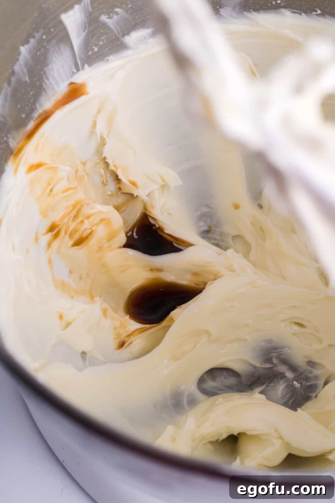 Cream cheese, vanilla extract, and powdered sugar being mixed in a bowl until smooth.