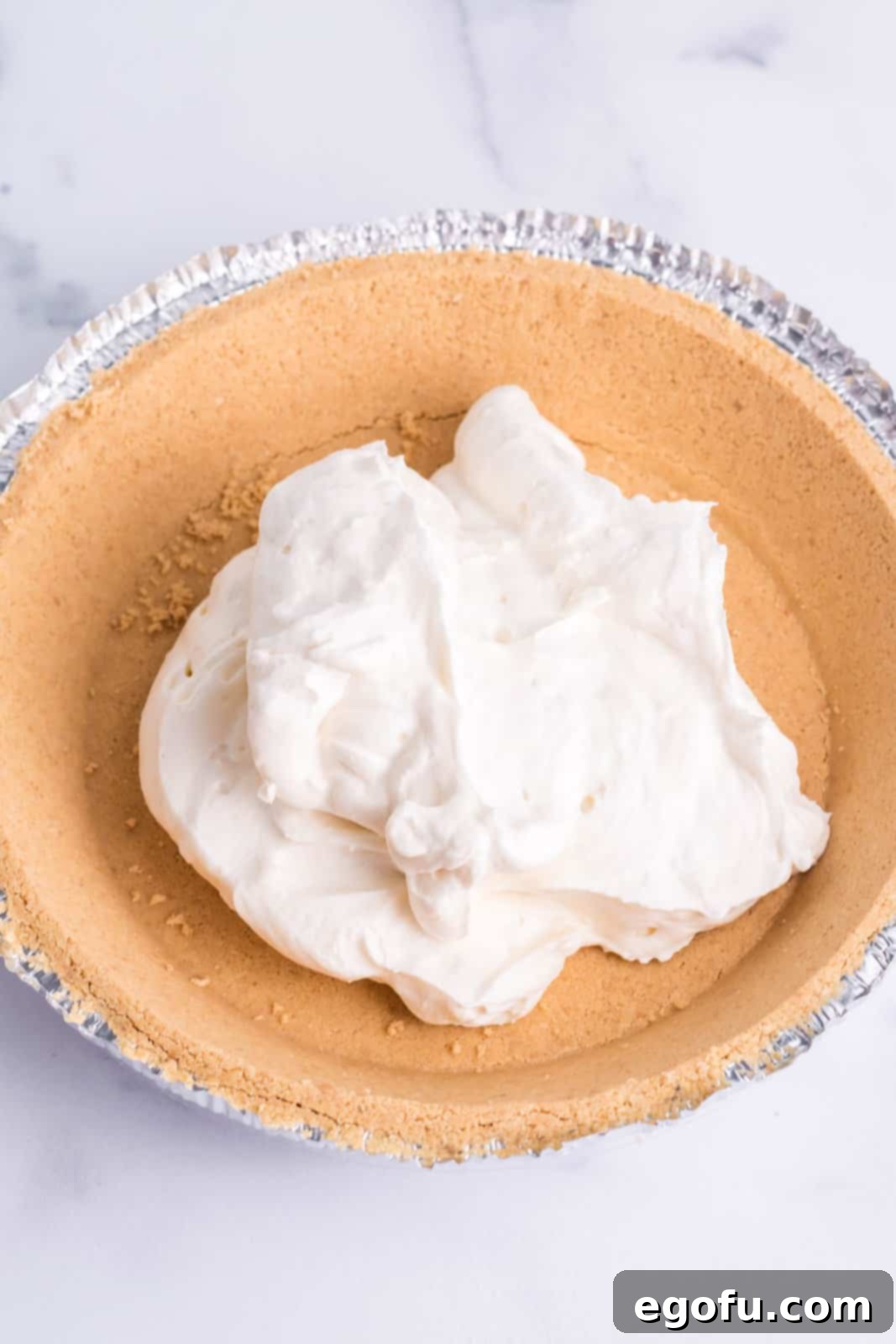 Cream cheese filling being gently poured into a graham cracker crust.