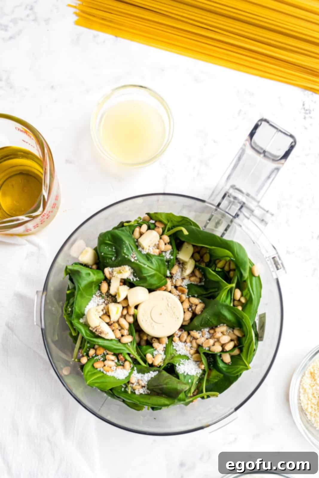 Fresh basil, garlic, pine nuts, salt, and pepper being pulsed in a food processor to start the pesto sauce.