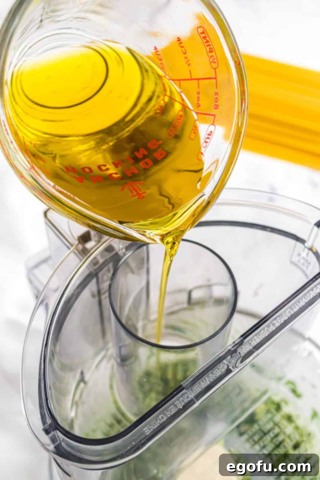 Olive oil being poured into the food processor with the basil mixture, ready to be blended into pesto.