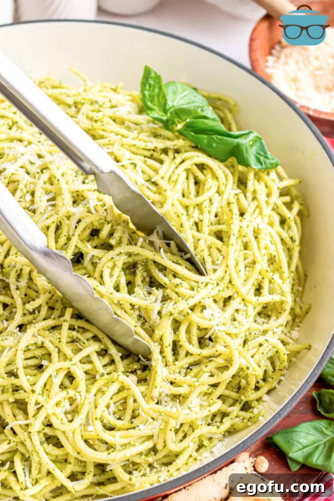 Tongs gently tossing a bowl of spaghetti coated in rich green pesto sauce, ready for serving.