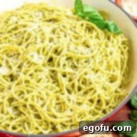 A beautiful bowl of pasta with homemade pesto sauce, garnished with a sprig of basil.
