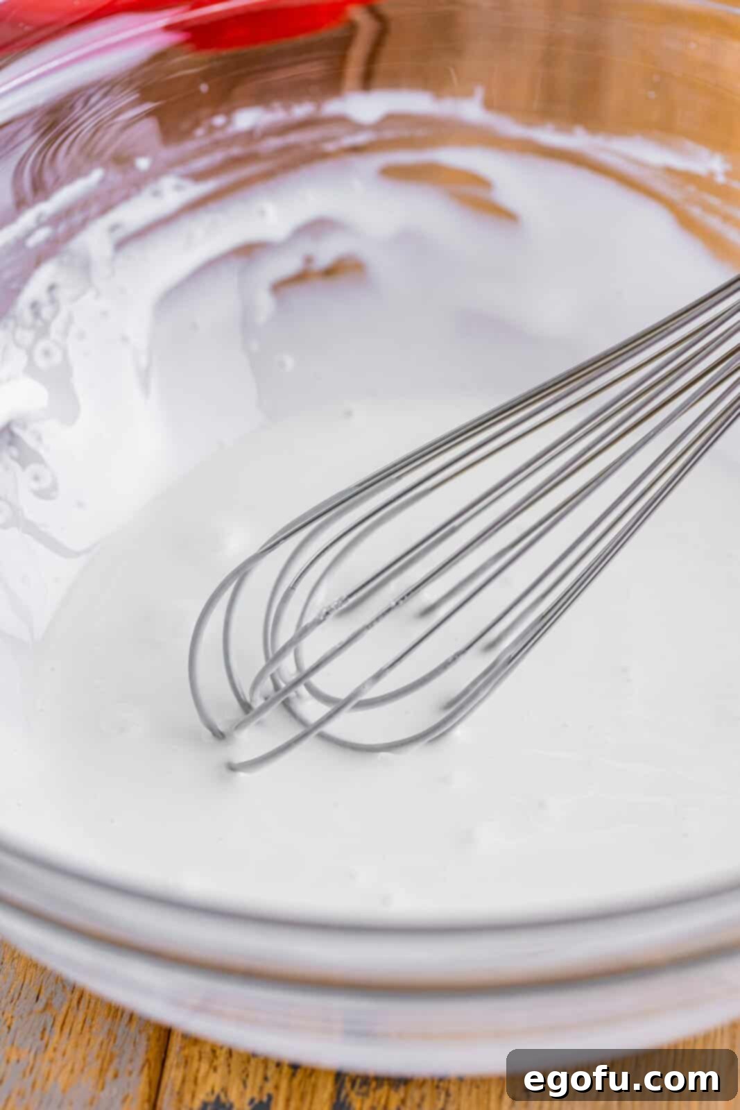 A mixing bowl with a whisk, whisking the powdered sugar, vanilla, and milk together. 